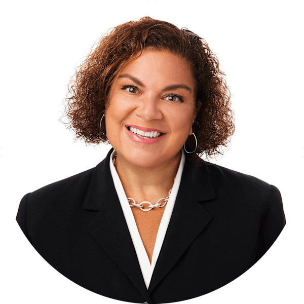 A woman with short, curly brown hair smiles at the camera. She wears a white blouse and black jacket.