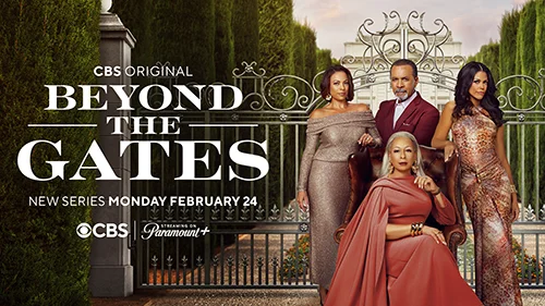A woman in a long gown sits on a tall leather chair. Two women and a man in formal attire stand behind her. They all stand in front of an iron gate. Trees and a white mansion in the background.