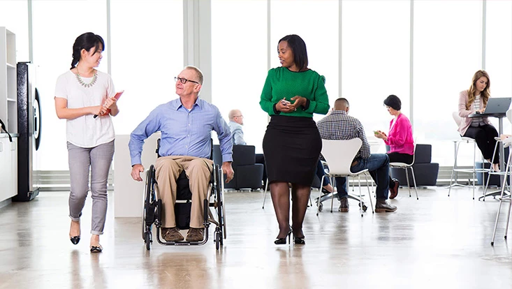 Two women are walking on either side of a man in a wheelchair.