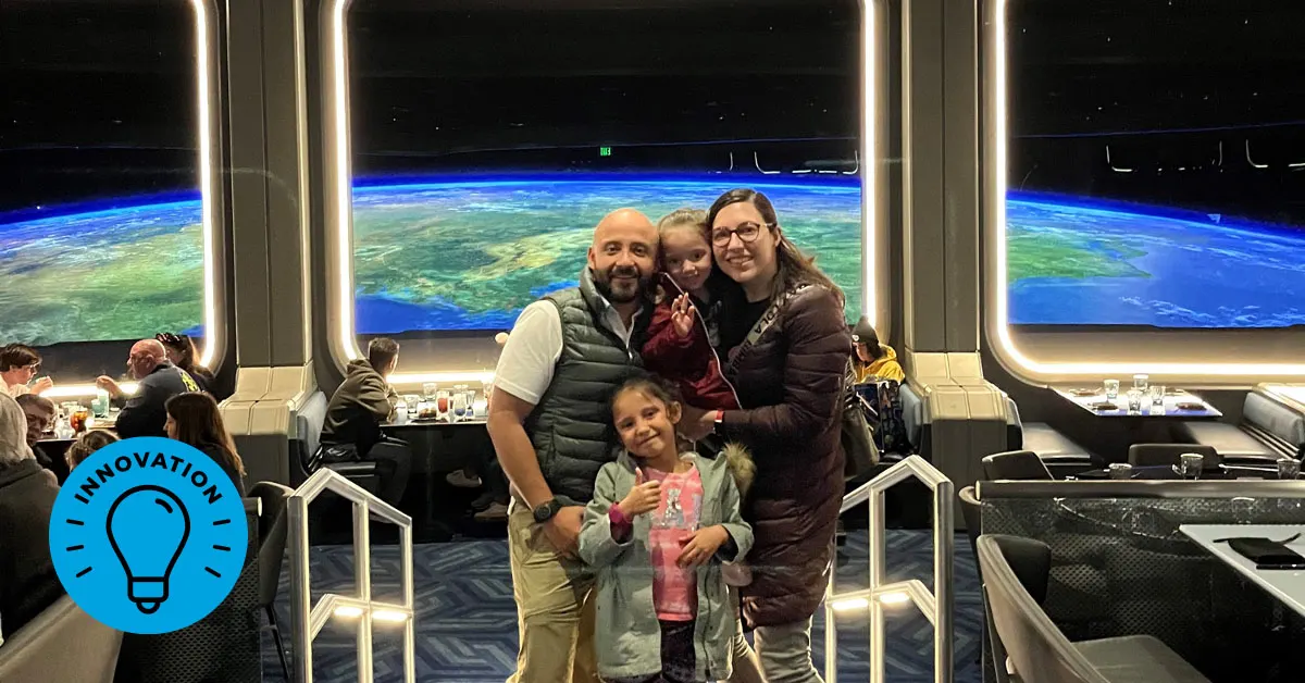 An adult woman, adult man, and two young girls pose together in the Space 220 Restaurant at the Walt Disney World Resort. The restaurant windows simulate a panoramic view of Earth from outer space.