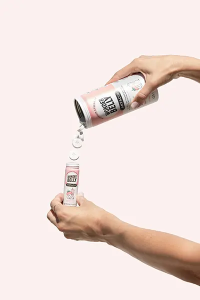 A woman’s hands pouring Wonderbelly antacid from a full-sized canister to a mini canister