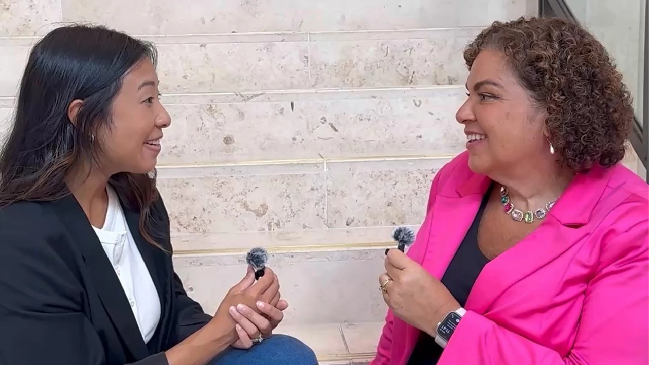 A video of two women sitting on a white stone staircase and having a conversation. 