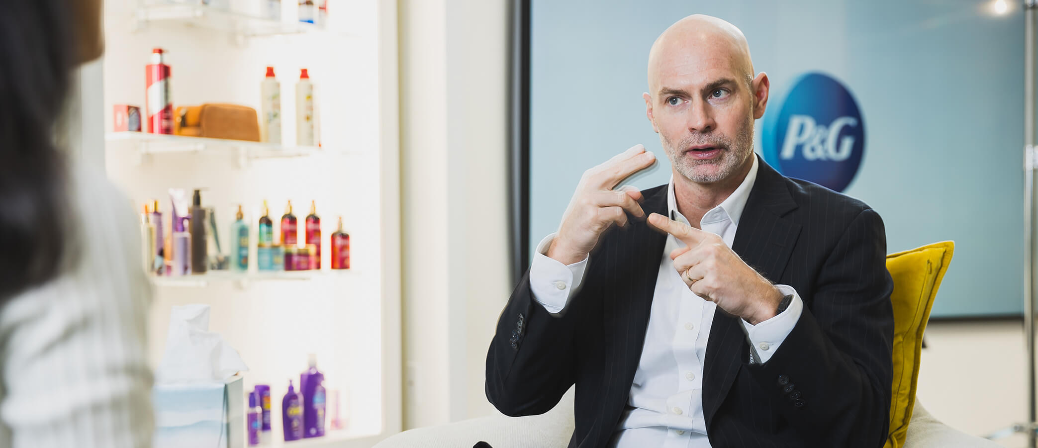 A man in a white shirt and black jacket looks off-camera as he uses sign language.