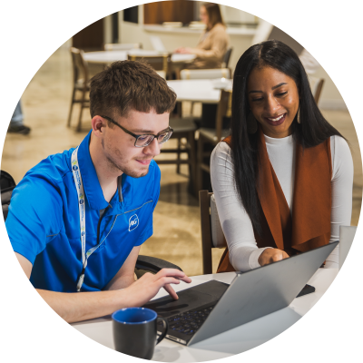 Two P&G employees sitting at a desk smiling and looking at a laptop in one of P&G's meeting spaces.