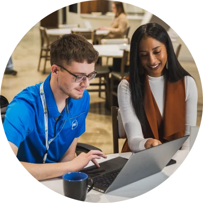 Two P&G employees sitting at a desk smiling and looking at a laptop in one of P&G's meeting spaces.