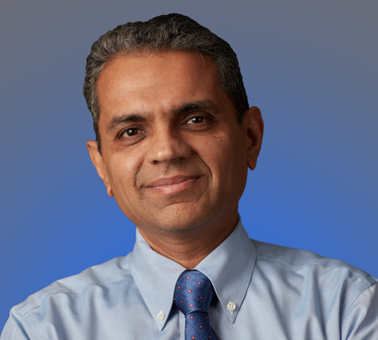 Bala Purushothaman, Chief Human Resources Officer slightly smiling toward the camera. He is wearing a light blue shirt with a dark blue tie.