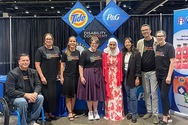 A group of people smiles in front of a conference booth display featuring P&G and Tide logos and multicolored text that says, “Disability Confident.”