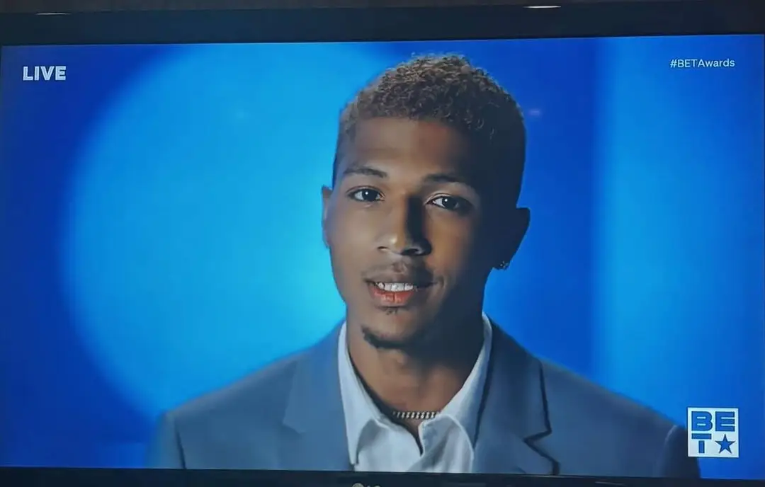 Close-up of a speaker in a suit shown on a television broadcast with “LIVE” and “BET Awards” graphics on a blue background.