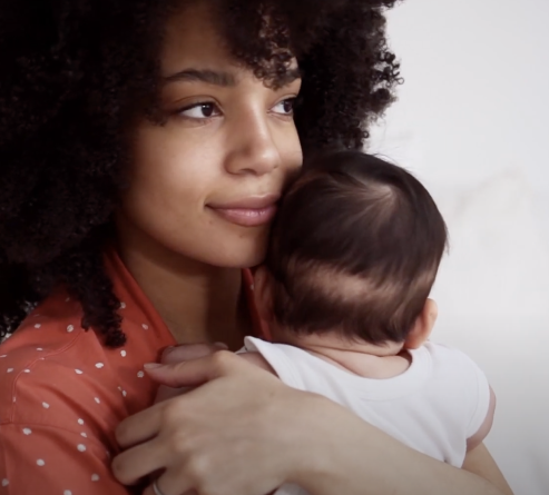 Young African American woman with curly hair holding and cuddling with her baby.