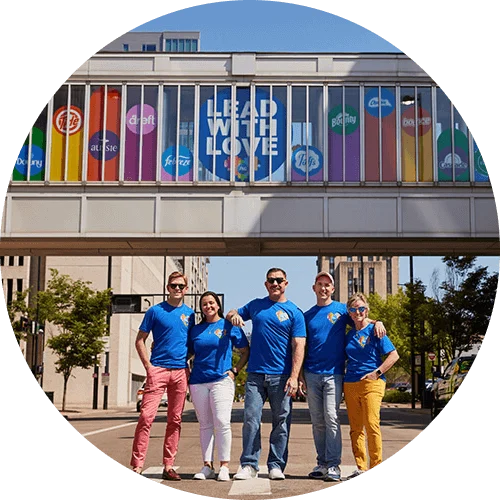 Five members of P&G’s “GABLE employee resource group stand in front of a bridge with a sign that reads, “Lead with Love.”