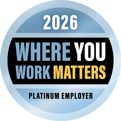 A blue circular badge with a black band and bold text in blue, yellow, white and black reads, “2026. Where you Work Matters, Platinum Employer”