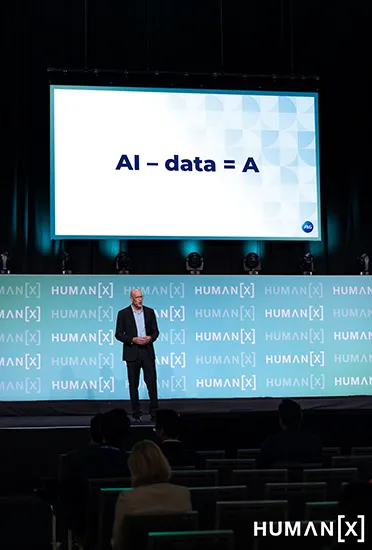 A man in a black suit stands on a large stage.