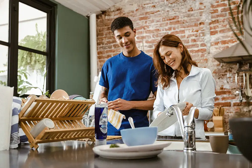 A man and woman stand in a kitchen. They are washing dishes.