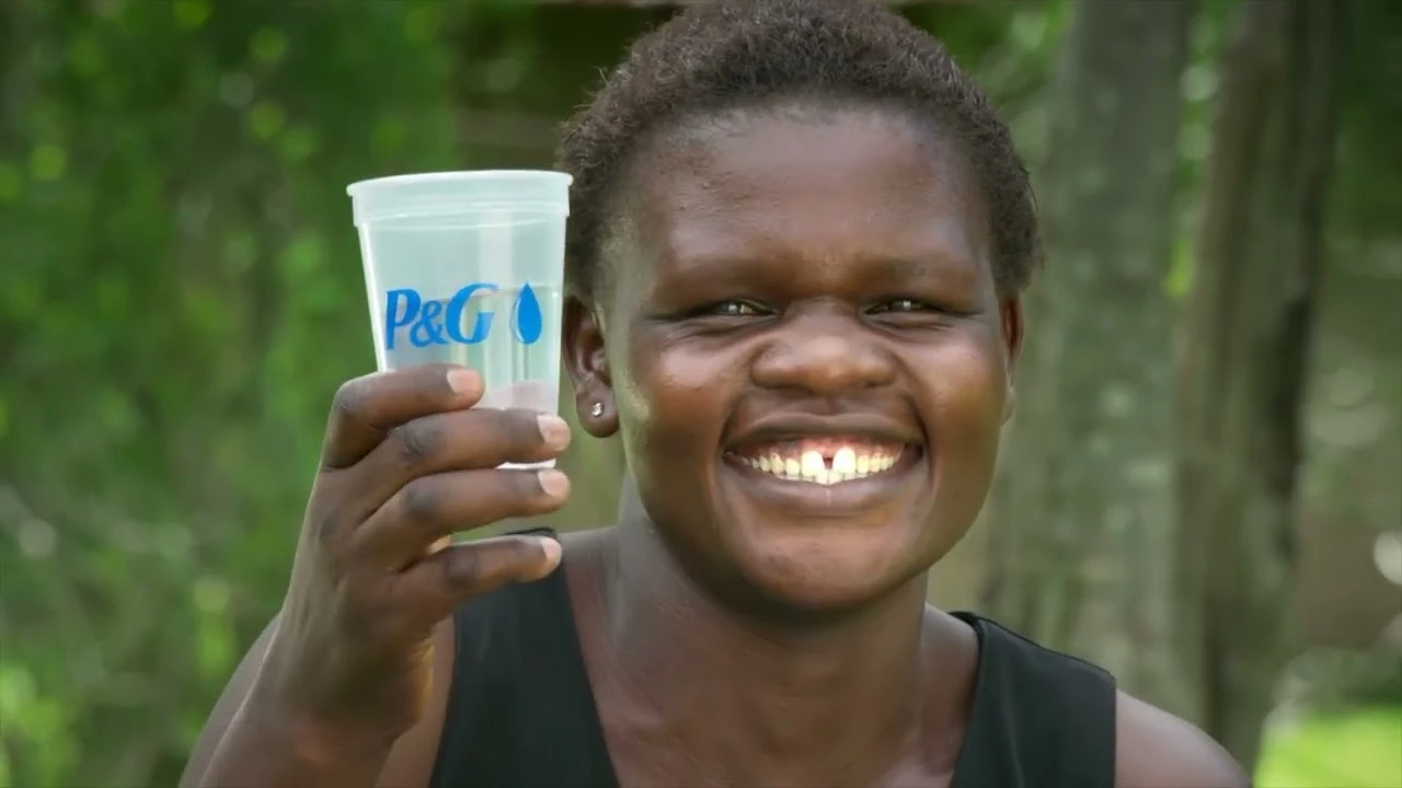 A young African boy smiles as he holds up a plastic cup of water.