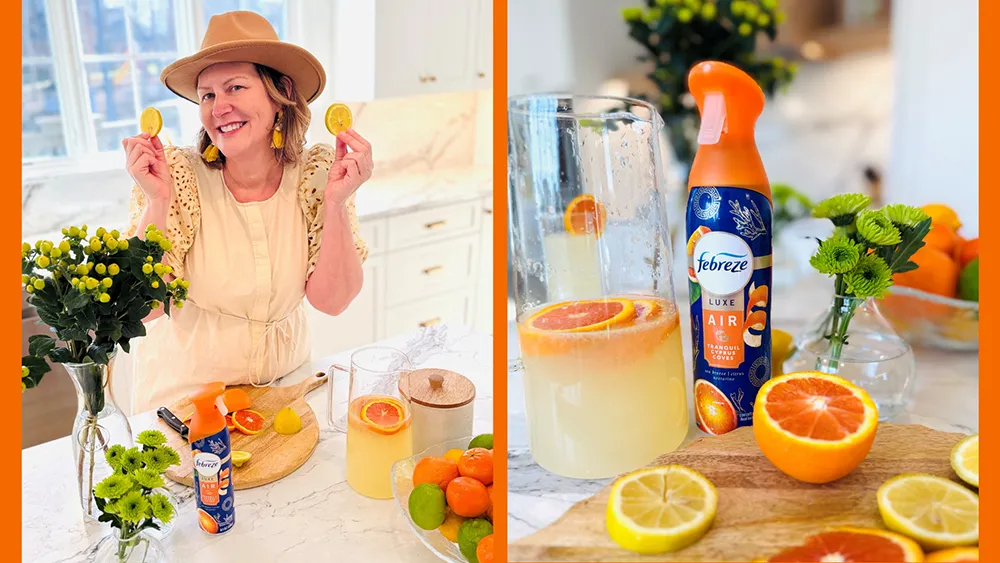 Michelle Hagan, a woman in a hat, playfully holds lemon slices in a bright kitchen setting, with a Febreze Tranquil Cyprus Coves air spray, fresh citrus fruits, and flowers on the counter.