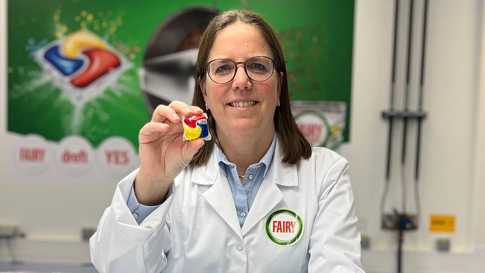 Katrien Hellings in a white lab coat, holding out in front of her a dishwasher cleaning packet