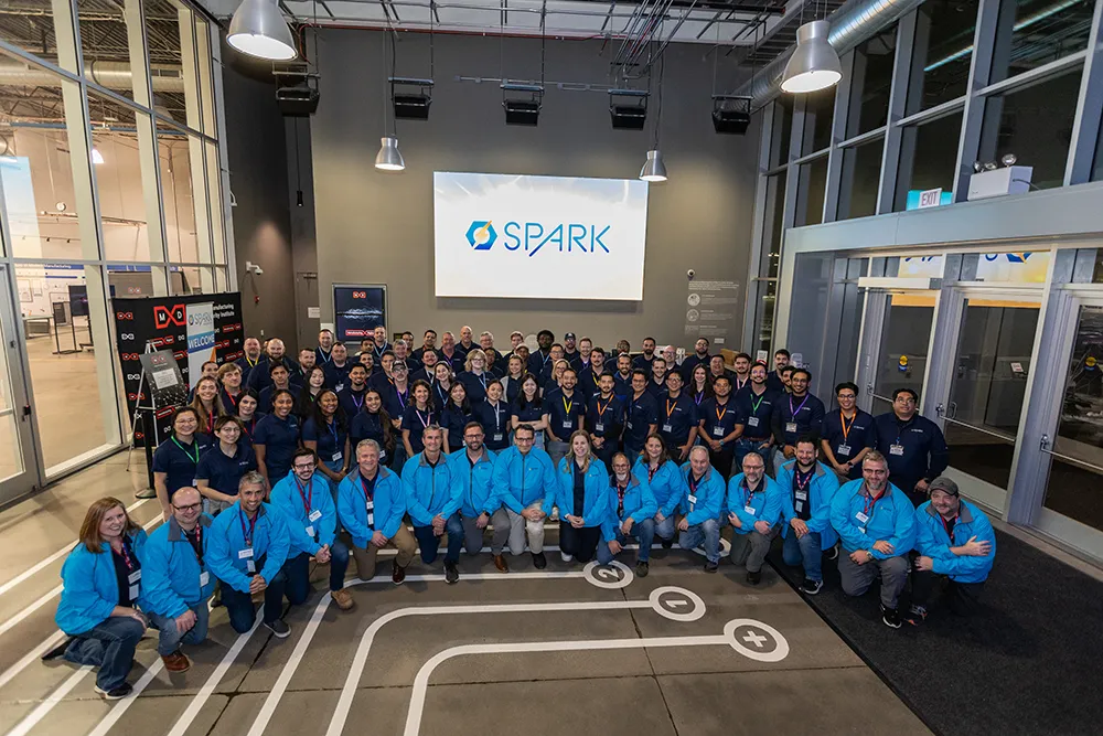 A group photo of manufacturing employees with a SPARK sign on the wall in the background