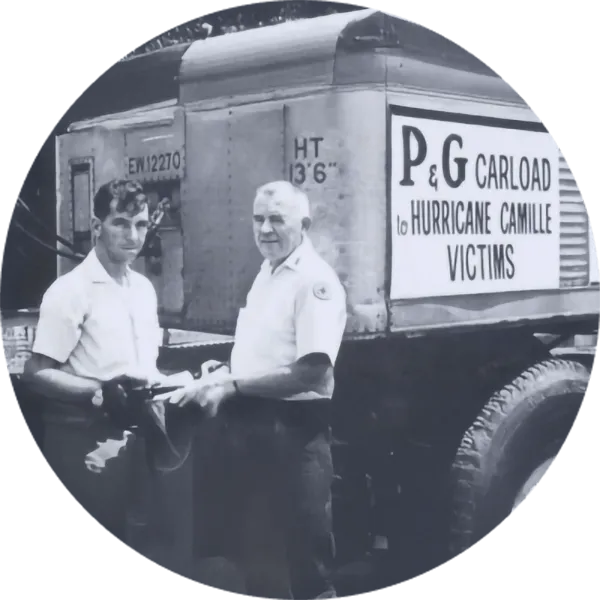 Historic photograph of two people standing beside a truck labeled 'P&G carload to Hurricane Camille victims'
