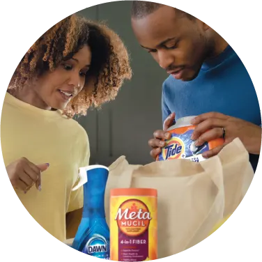 A man and woman are unpacking a bag of groceries, including Tide, Dawn and Metamucil.