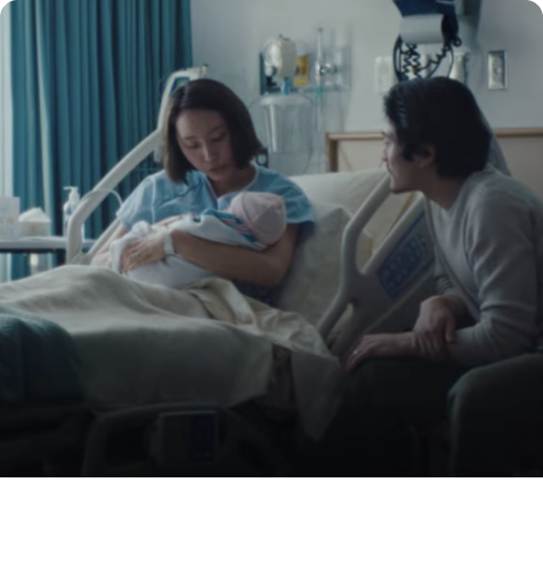 Woman lying in hospital bed holding her baby. Dad sitting beside them.