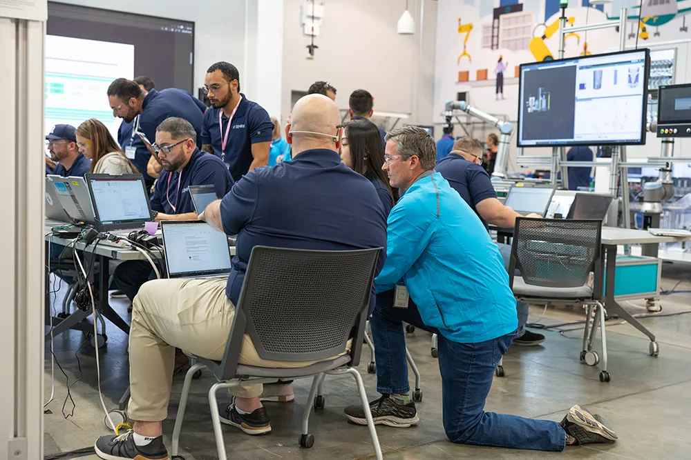 An instructor kneels next to a participant sitting in a chair with a computer on his lap
