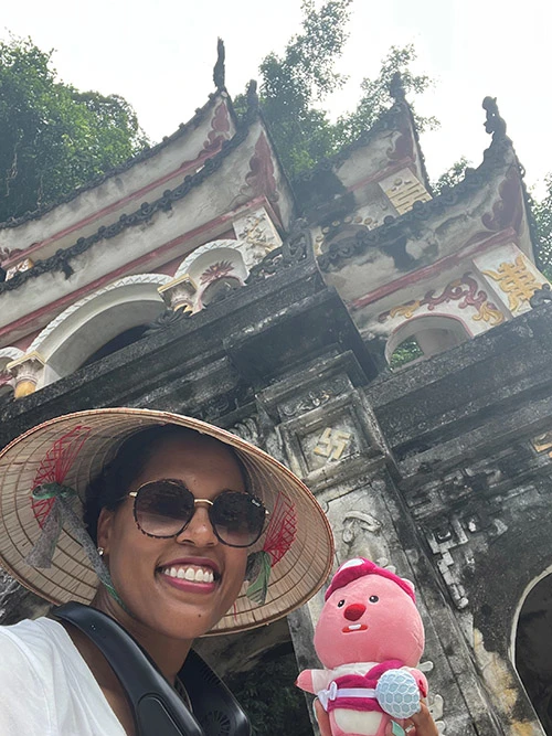 A black woman in a hat and sunglasses smiles as she poses in front of a temple in Vietnam.