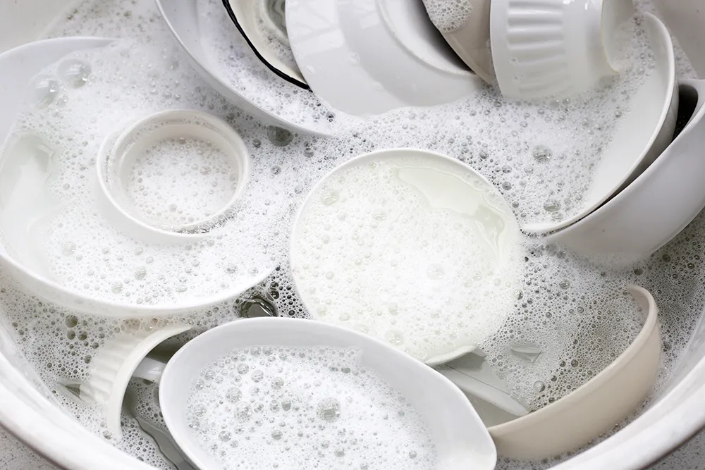 A sink full of white dishes and bowls submerged in soapy, bubbly water.