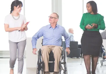 A man in wheelchair and two women in the office talking
