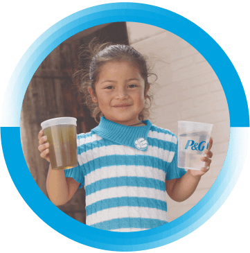 A young girl with brown hair is holding two cups in her hands. One cup is full of a brown, dirty water and the other is full of clean water. The cup with clean water has the P&G logo on it.