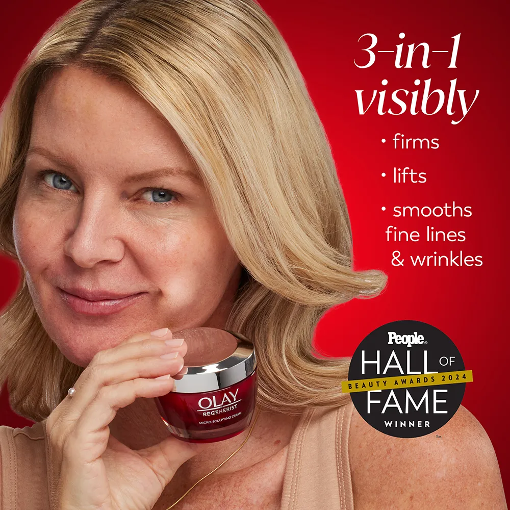 A blonde woman with shoulder-length hair smiles against a red background while holding a dark red jar of face cream.
