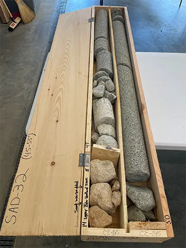 Inside a wooden box, geological core samples are organized, showing different types and sizes of rocks collected for study.
