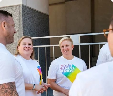 People standing looking toward each other and waring white T-shirts with colourful Can't Cancel Pride logo.