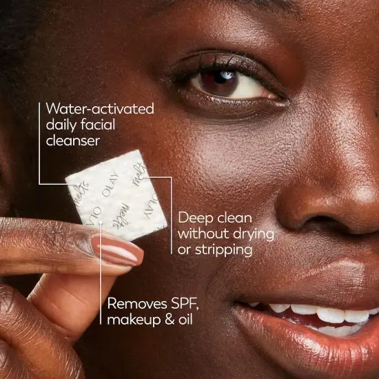 A woman holds an OLAY Cleansing Melt tile in front of her face; the image is labeled noting the product’s features.