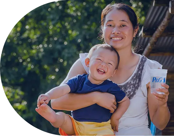 Thai woman in a white shirt holds a P&G cup filled with clean water and a smiling baby in a navy blue shirt on her lap.