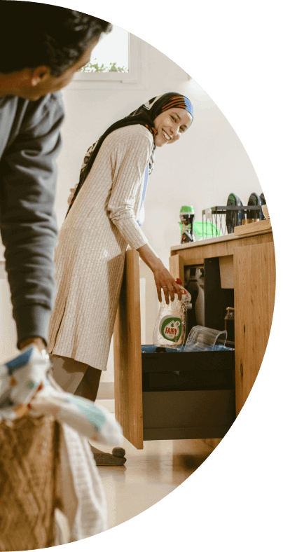 A woman smiles at her husband while placing an empty bottle of Fairy Dish Washing Liquid in the recycling bin