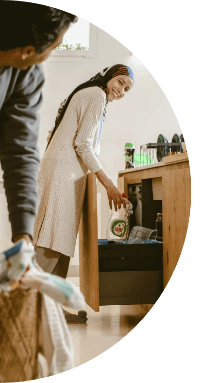 A woman smiles at her husband while placing an empty bottle of Fairy Dish Washing Liquid in the recycling bin