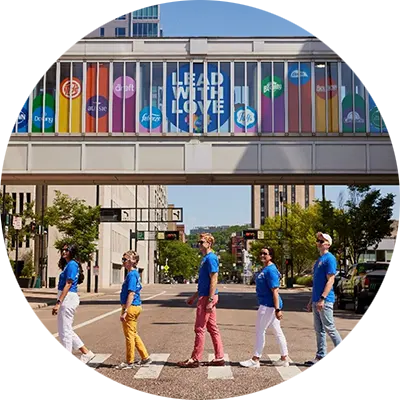 P&G employees cross street in front of rainbow Lead with Love sign featuring P&G brands.