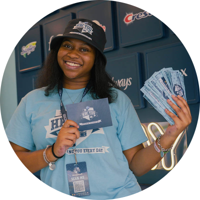 A young, black female college student holds up a blue card and P&G prize money. She is wearing a light blue t-shirt.