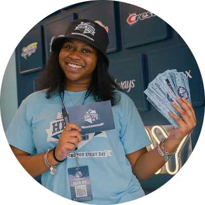 A young, black female college student holds up a blue card and P&G prize money. She is wearing a light blue t-shirt.