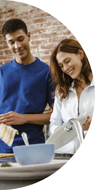 A man and woman smile as they wash dishes together
