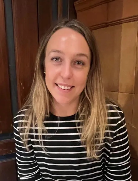 Young woman with long, blonde hair smiling. She wears a black and white striped shirt.