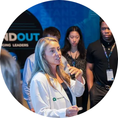 A woman gives a presentation while several attendees stand nearby at a leadership event.