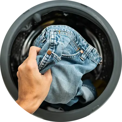 Hand placing denim jeans into a washing machine drum