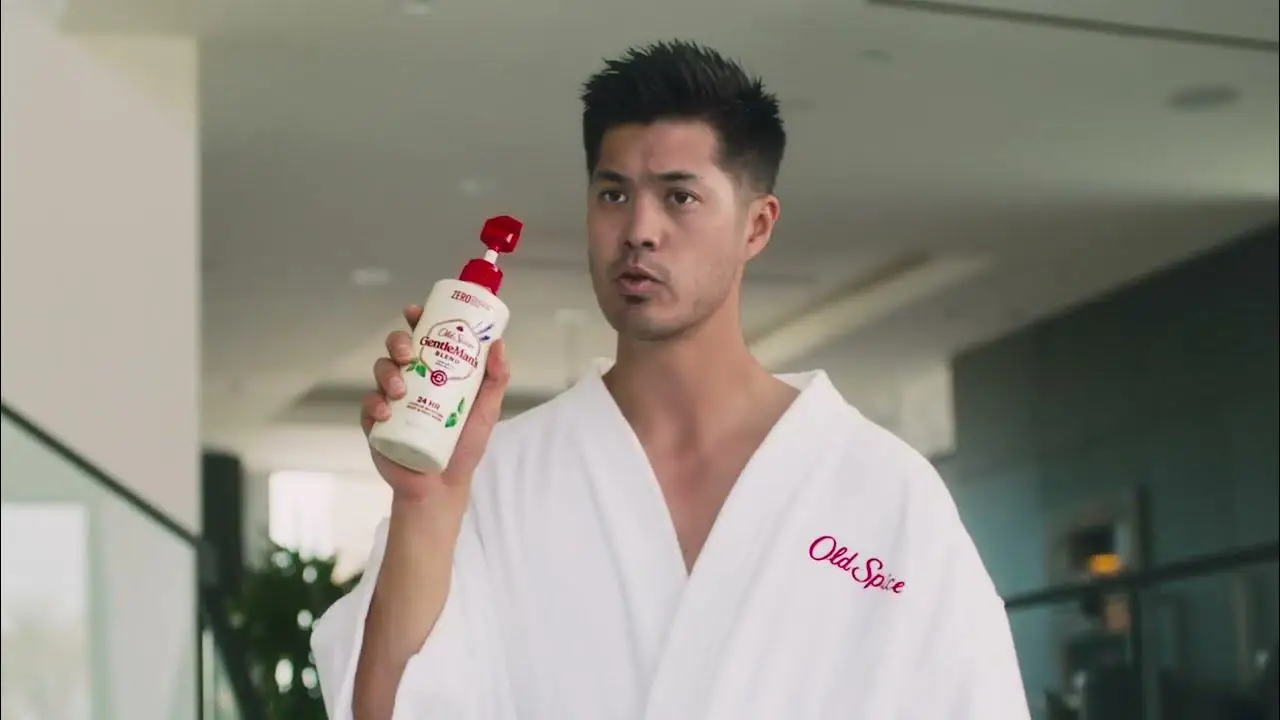 Person in an Old Spice robe holding a bottle of Old Spice product in an indoor setting.