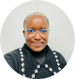 A black woman with short blonde hair wears glasses and a black sweater as she smiles directly at the camera.