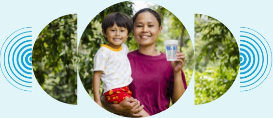 A mother in a pink shirt smiles as she holds her child with a giant grin in one hand and a P&G branded cup of clean water in her other hand