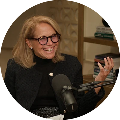 Katie Couric smiling in a room with a microphone
