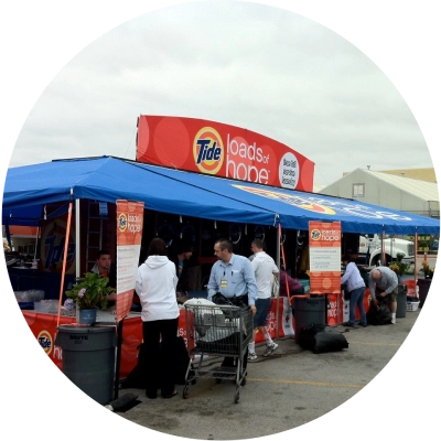 A blue tent with "Tide Loads of Hope" signage, where people are interacting and sorting laundry bags.