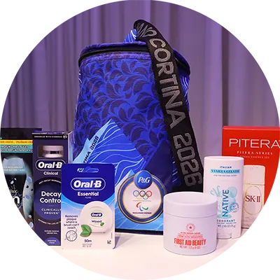 A collection of P&G products displayed on a white surface against a purple curtain backdrop. Products include a blue patterned bag with "Milano Cortina 2026" on the strap and the P&G Worldwide Olympic and Paralympic Partner medallion.