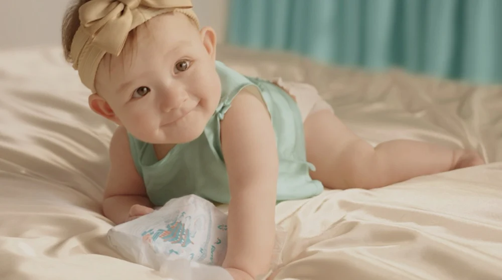 Baby crawling on a bed next to a Pampers diaper